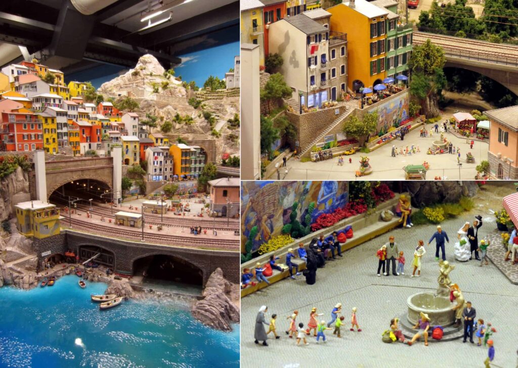 This detailed model of a coastal town, reminiscent of Miniatur Wunderland in Hamburg, Germany, features colorful buildings against a mountain backdrop. Scenes include boats on the blue sea, a bustling square, and a market with miniature figures near a charming fountain.