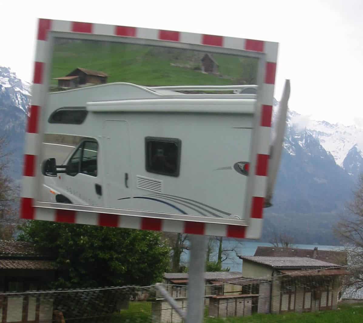 Reflection of a motorhome in a street mirror with snow capped mountains in the background on a misty day travelling Europe.